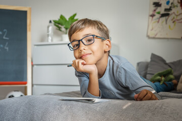 One schoolboy laying on bed in his room at home doing homework, learning indoor concept 