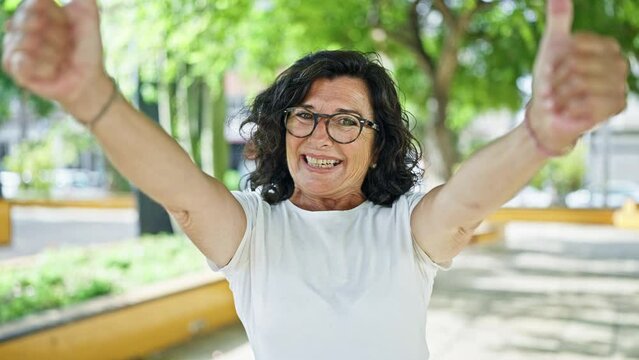 Middle age hispanic woman smiling confident doing ok sign with thumbs up at park