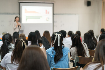 Rear view of college students listen to teacher teaching and explaining lesson in classroom