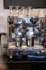 The barista prepares fresh coffee in the coffee machine in the morning in the cafe. There are coffee cups on the table for customers. Coffee machine close-up