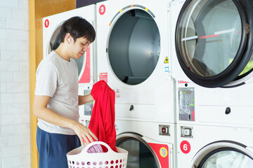 Asian man putting an used or dirty clothes in the self-service automatic laundry washing machine.