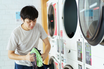 Asian man putting an used or dirty clothes in the self-service automatic laundry washing machine.