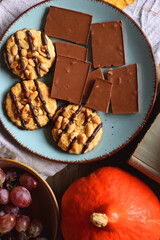 Cup of tea or coffee, plate with cookies and chocolate, dried oranges, bowl of grapes, vintage books, pumpkins and autumn leaves on the table. Autumnal hygge. Top view.