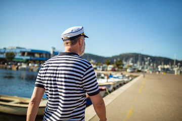 Fototapeta na wymiar Mature man standing near the sea dressed in a sailor's shirt and hat.