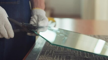 Medium close up of hands of craftsman separating part of cut glass while sitting at working place at glassware studio