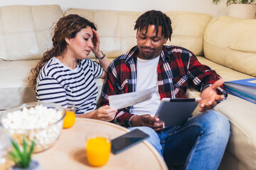 Multiracial couple at home analyzing their finance with documents and laptop.