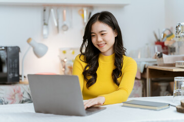 Obraz na płótnie Canvas Beautiful Asian woman smiling happily relaxing using laptop technology Take notes Drink a relaxing hot drink while sitting on the table in your room at home.