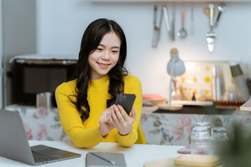 Beautiful Asian woman smiling happily relaxing using laptop technology Take notes Drink a relaxing hot drink while sitting on the table in your room at home.