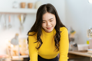 Beautiful Asian woman smiling happily relaxing using technology of laptop computer Take notes Drink a relaxing hot drink while sitting on the table in your room at home.