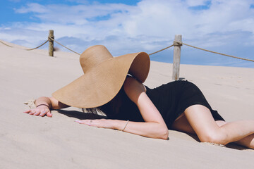 European Girl in a black dress and hat posing on the golden sand of the desert dunes