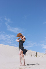 European Girl in a black dress and hat posing on the golden sand of the desert dunes