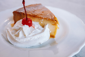flan cake with whipped cream and a red Mero chino cherry on a white plate