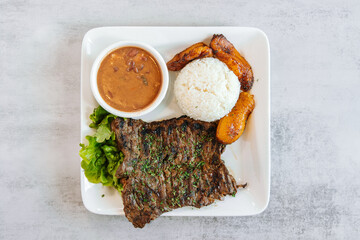 Columbian food grilled skirt steak with a side of rice plantains and refried beans