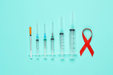 Red AIDS awareness ribbon and syringes on a blue background. Medicine concept