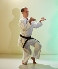 An adult man with a black belt performs formal exercises against a colored background with yellow...