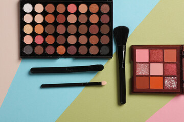 Makeup palettes with brushes on a colored background. Top view