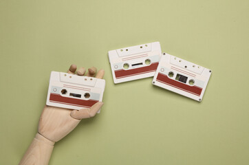 Wooden hand holding retro 80s audio cassettes on green background