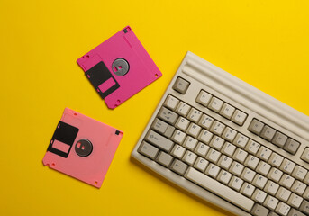 Retro keyboard and floppy disks on yellow background. Top view