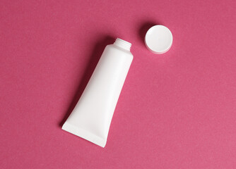 Opened white cream tube on pink background. Top view