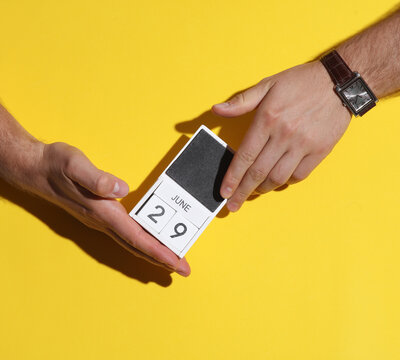 Man's hand holding wooden block calendar with date June 29 on yellow background