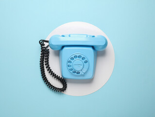 Retro blue painted rotary phone on blue background with white circle. Top view. Minimalism