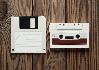 Retro 80s floppy disk and audio cassette on wooden background. Vintage technology. Top view.