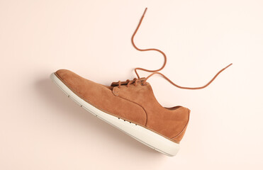 Men's suede shoe with untied laces on beige background