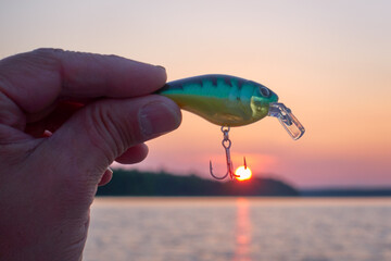 Male fisherman holding a small wobbler lure that hooked a setting sun on a lake in Western Finland.