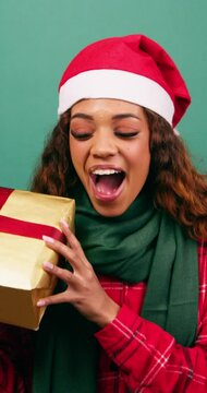 Excited young woman shakes Christmas gift, guessing what is inside, Studio