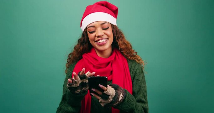 Beautiful young woman in Santa hat texts and uses phone laughing, Xmas studio