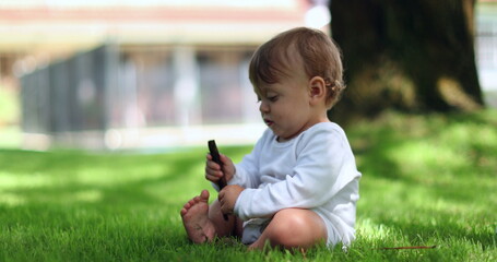 Cute baby sitting outside playing with stick and toes on lawn