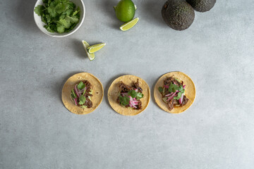 Mexican tacos with pulled pork, red onion, limes, and avocados. cement background