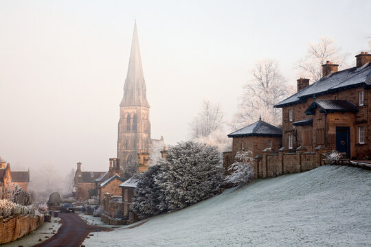 A tall church steeple in the fog within a neighbourhood in winter; Edensor, derbyshire, england
