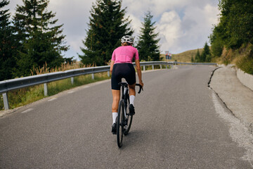 Close-up back view of a female cyclist during a ride. Woman cyclist is wearing cycling kit and a helmet while riding her gravel bicycle through stunning Romanian mountain landscapes. Bucegi Mountains