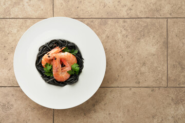 Black spaghetti pasta shrimp on black plate on light concrete table background. Squid ink pasta with prawns. Pasta seafood. Top view on black stone table. Mediterranean traditional cuisine dish.