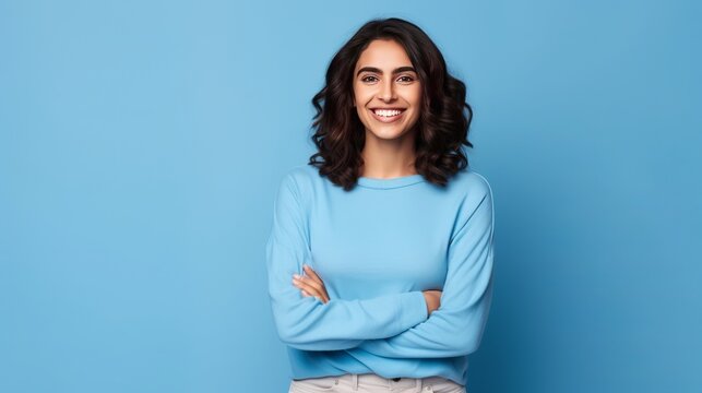 Young Caucasian woman smiling and posing with her arms at her hips on an isolated blue background.