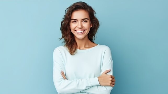 Young Caucasian woman smiling and posing with her arms at her hips on an isolated blue background.