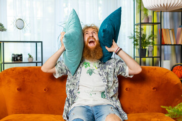 Repair work at neighbors. Irritated Caucasian man cover ears with pillows annoyed by noisy loud...