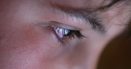 Child eye close-up tablet screen display. Young boy eyes staring at blue light at night