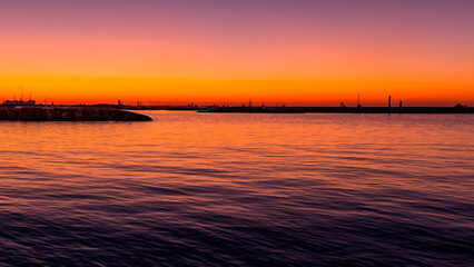 orange sunset over sea and harbour with boats in distance