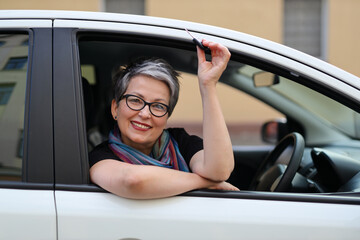 A mature, happy Caucasian woman, enjoying her journey in a new car, symbolizing independence and happiness.