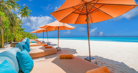 Panoramic holiday landscape. Luxury beach resort hotel. Leisure chairs loungers under umbrellas with palm trees, blue sunny sky. Stunning summer island seaside, travel vacation destination background