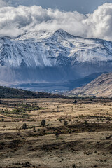 Landscape in Los Alerces National Park, Chubut, Argentina. A mountain range in warm tones with a background of cold blue Andes mountains covered in snow.