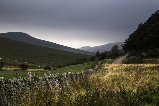 A Stone Fence With Wooden Posts Running Along A Road And The Sun Rising Over The Hills; Northumberland, England