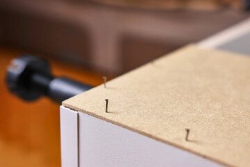 The back wall of the cabinet is nailed with nails and a hammer. Assembling cabinet furniture.
