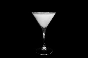 A martini glass with a white alcoholic beverage on an black background