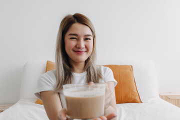 Fototapeta na wymiar Happy Asian Thai woman drinking coffee milk at apartment look at something.