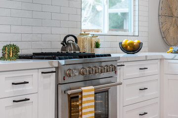 Modern kitchen details of large gas range with teapot and yellow and white towel near marble...