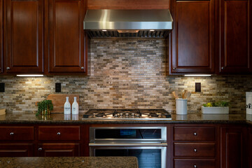 Kitchen details of granite counter, gas stove top, textured tile backsplash and dark wood cabinets.