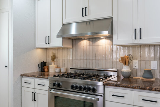 Contemporary kitchen details of large gas range, white cabinets, ceramic tile backsplash and marbled granite counter with kitchen accessories.